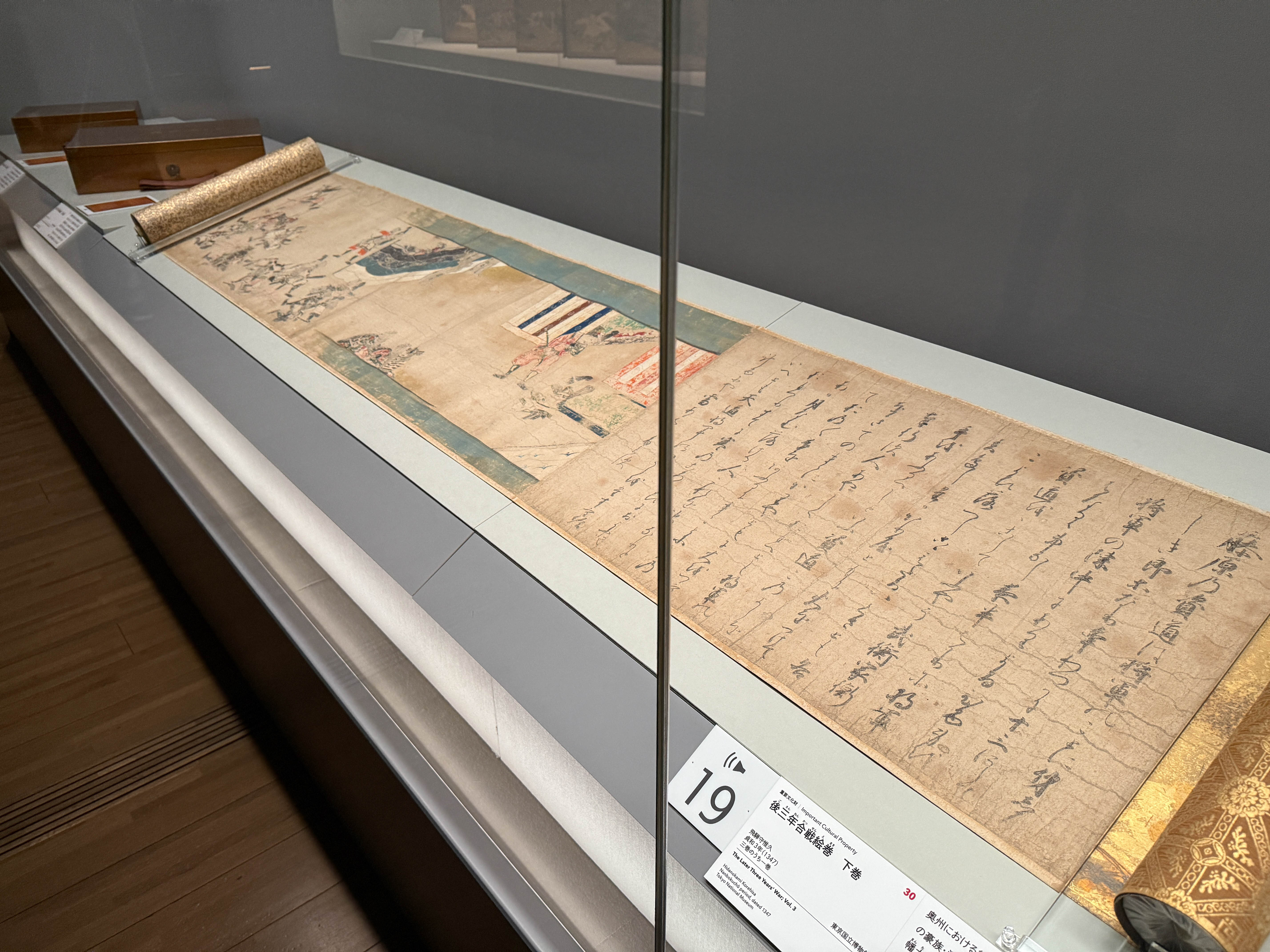 サントリー美術館「酒吞童子ビギンズ」会場より　（手前）重要文化財《後三年合戦絵巻》（部分）飛騨守久惟久　三巻のうち下巻　貞和3年（1347）東京国立博物館［通期展示、会期中場面替］