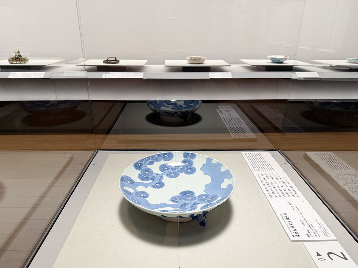 サントリー美術館「眼のごちそう 食器」会場より (手前)重要文化財《染付松樹文三脚大皿》鍋島 江戸時代 17~18世紀 サントリー美術館
